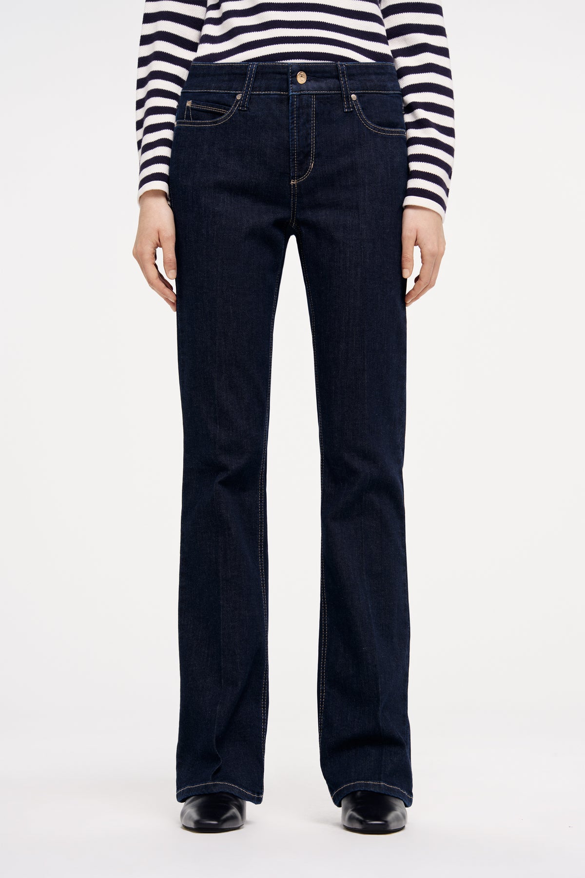 Dunkelblaue Flared-Jeans aus 93 % Baumwolle, 5 % Polyester, 2 % Elasthan, getragen mit gestreiftem Oberteil.