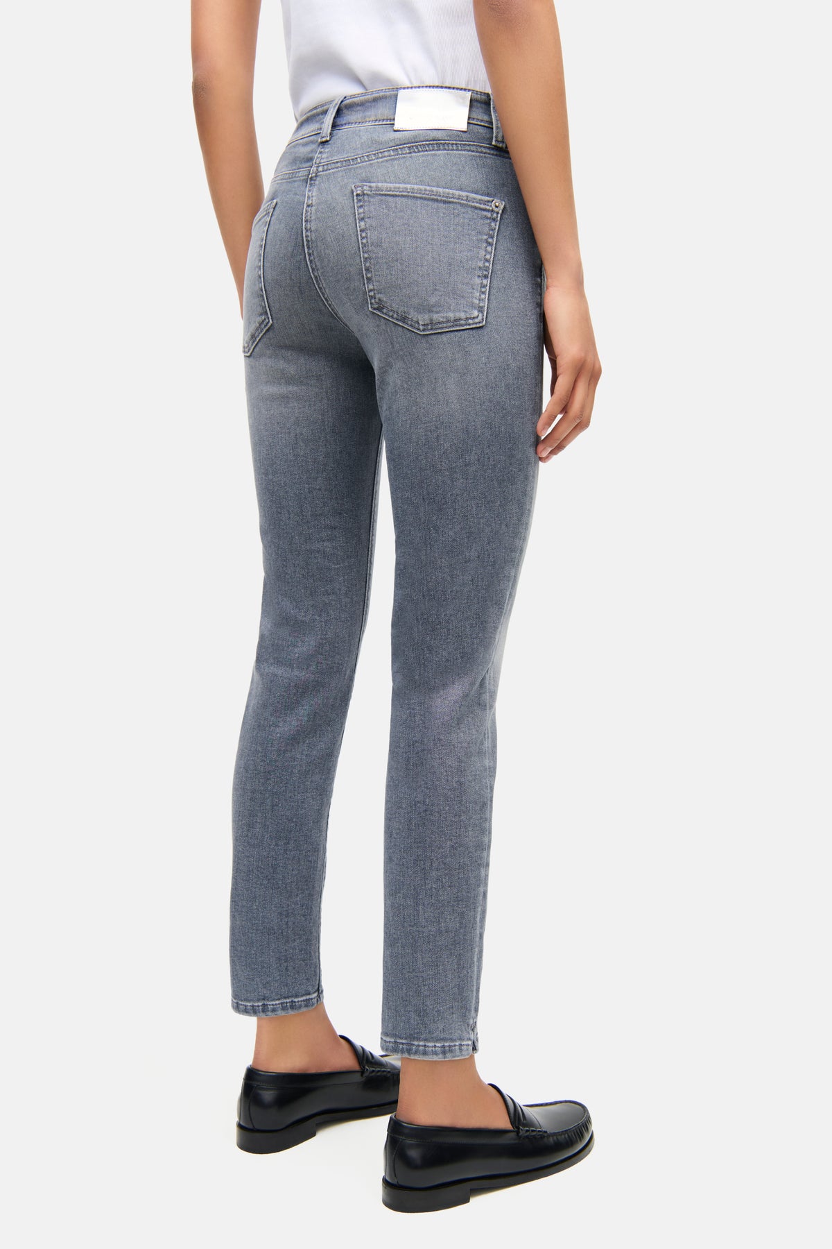 Graue Slim-Fit Jeans aus Denim, 92% Baumwolle, verkürzt. Getragen in einem urbanen Setting mit schwarzem Schuhwerk.