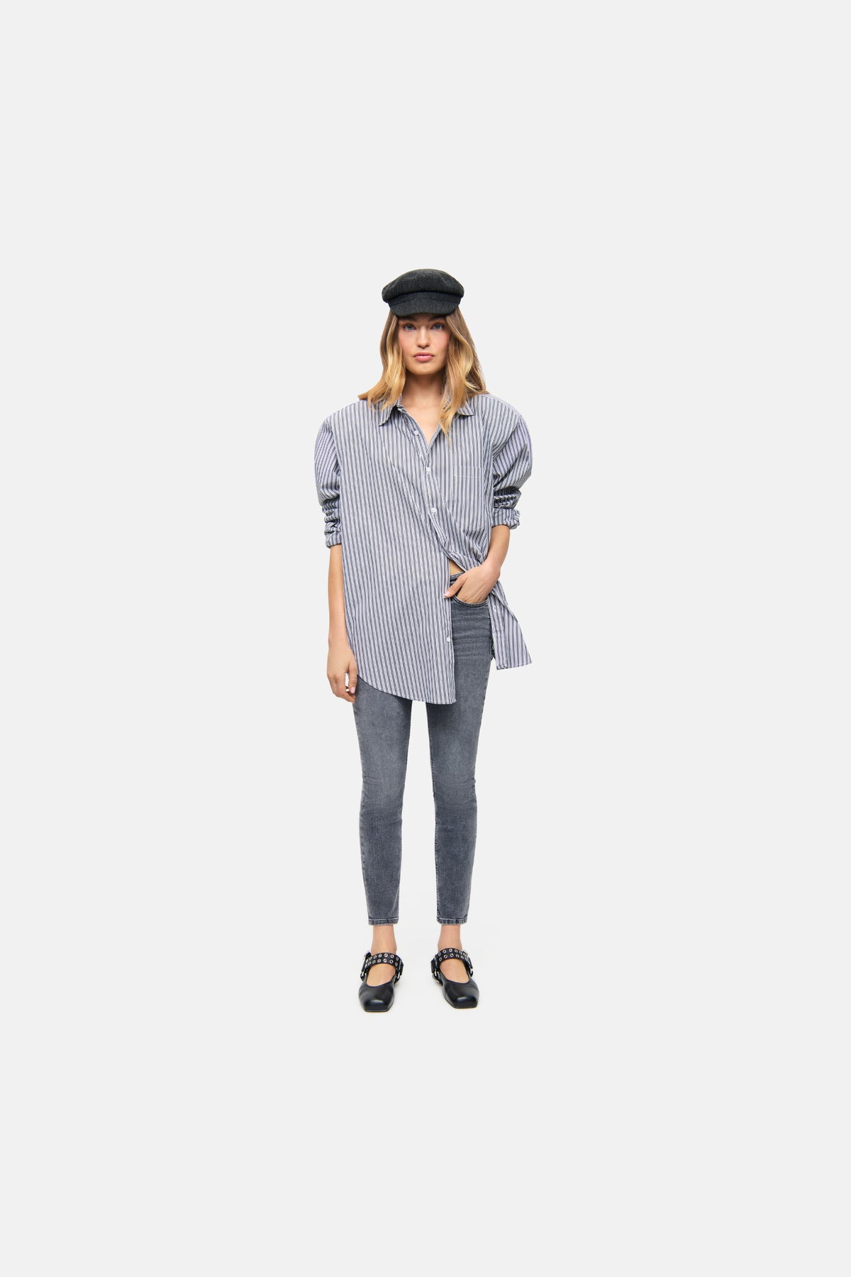 Graue Damenjeans, Slim-Fit, verkürzt, aus Superstretch-Denim. Getragen von Person in urbanem Setting mit Hemd und Mütze.