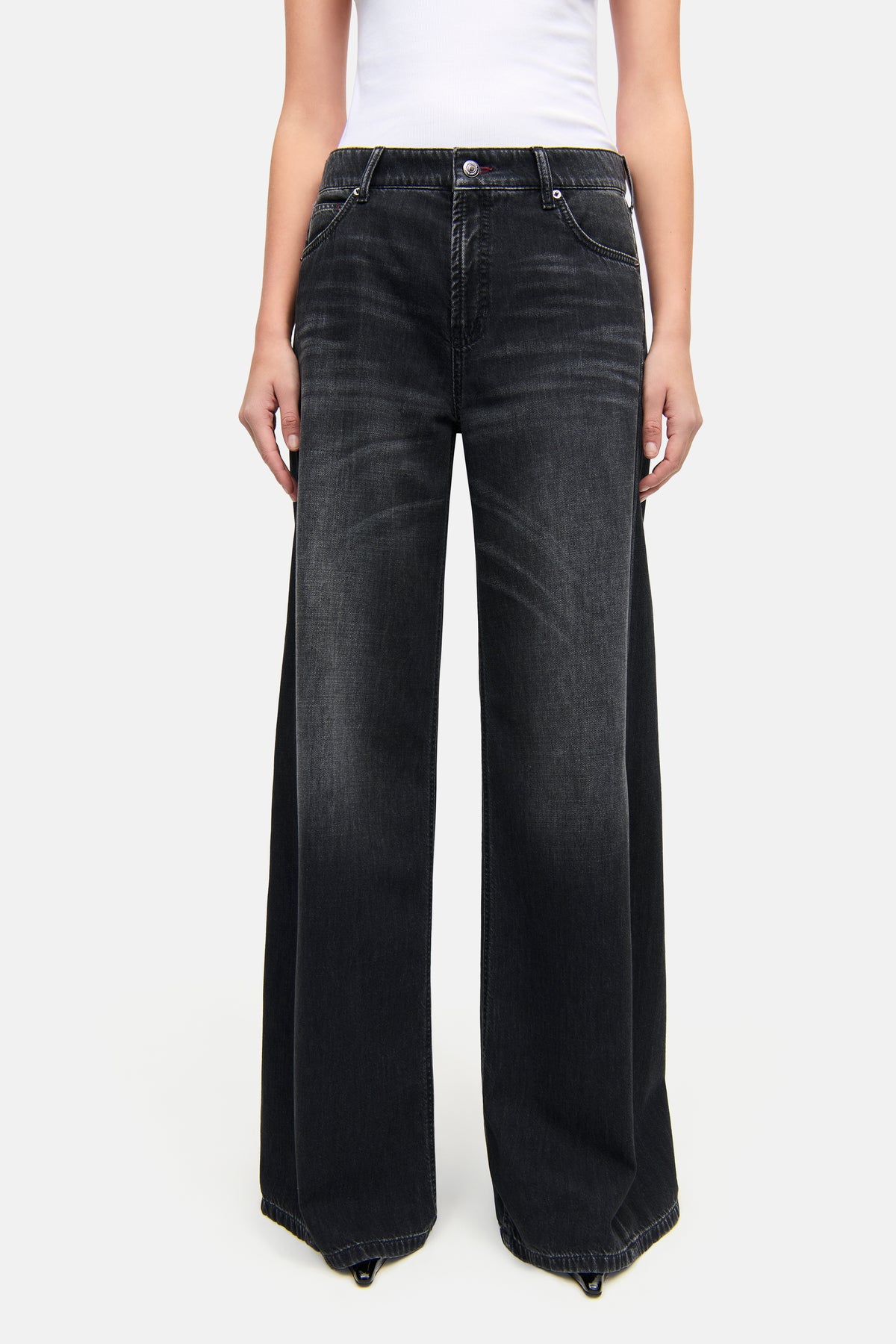 Schwarze Palazzo-Jeans aus Denim, erkennbar an seitlichen Einsätzen und 5-Pocket-Stil, getragen in einem minimalistischen Setting. Material: 92% Baumwolle, 6% Elastomultiester T400, 2% Elasthan.